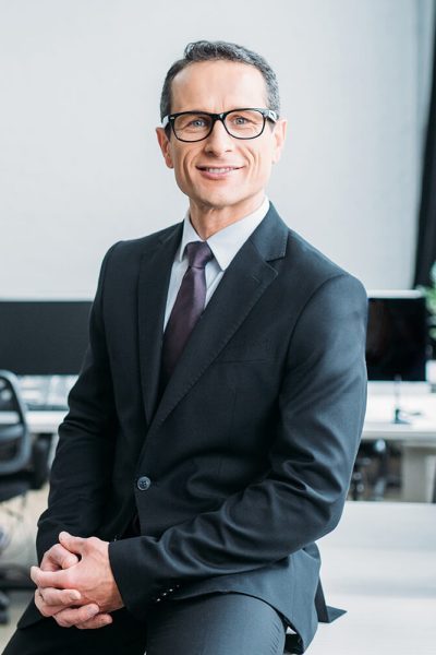 smiling-businessman-in-eyeglasses-sitting-on-table-V5AWVKC-rbbb2scgthwir9civuw9oenxt7sd0d40y5z9f69pio